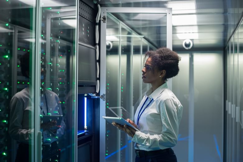 A female technician working on a tablet in a data center full of rack servers running diagnostics and maintenance on the system